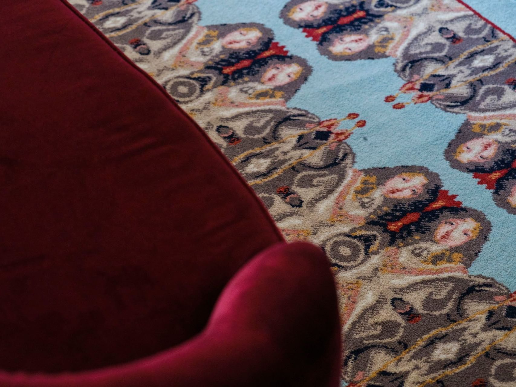 Red cushioned chair on a patterned rug with intricate, artistic design featuring faces and abstract shapes.