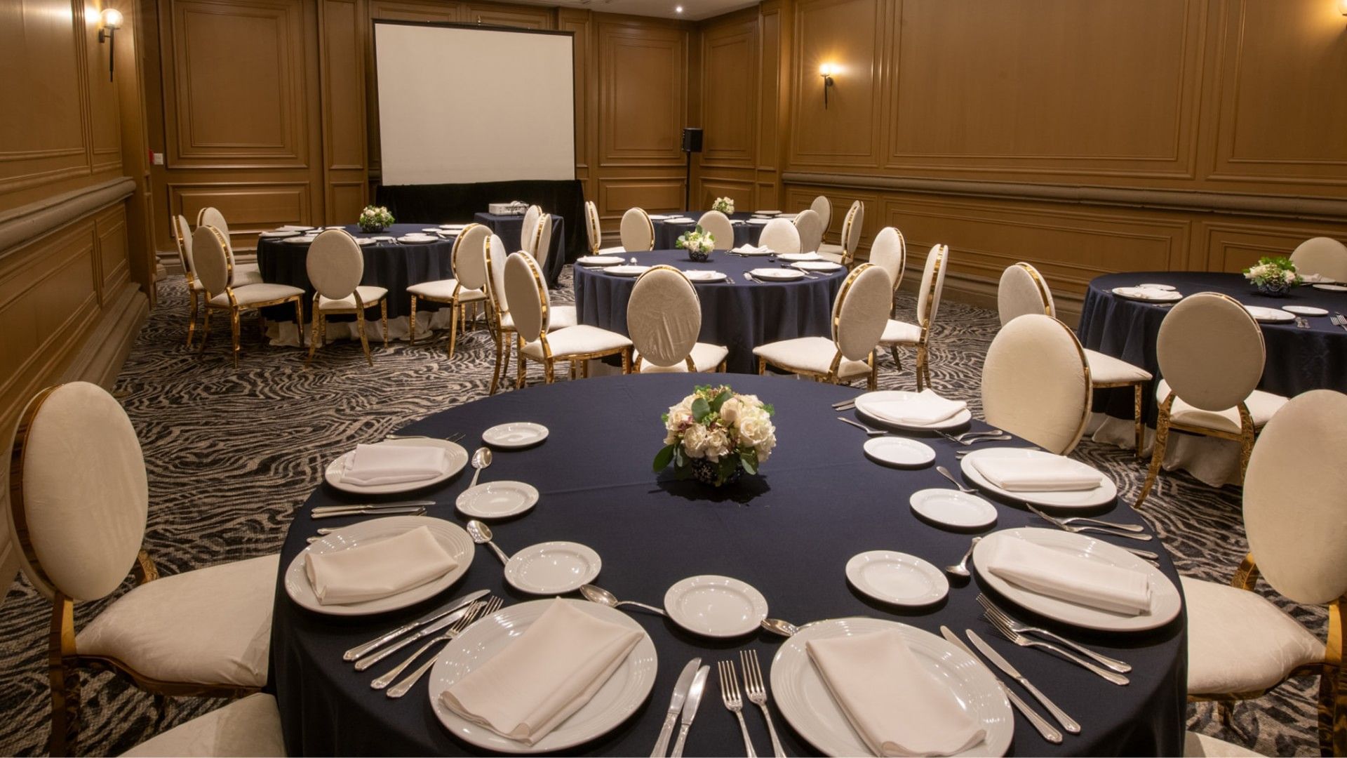 Salon Virreinal with navy blue tablecloths and a large projector screen at Quinta Real Monterrey