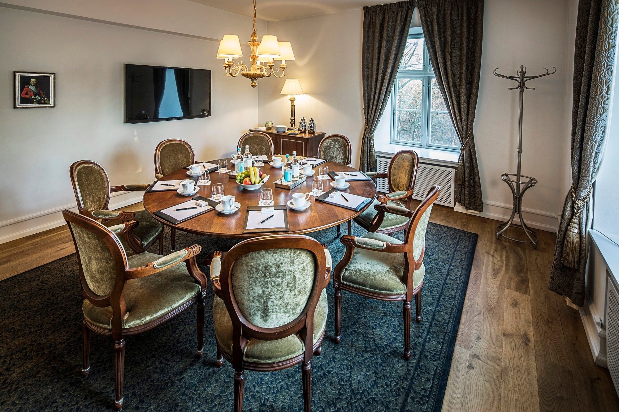 Sophisticated round wooden meeting table with green velvet chairs and formal settings at Warwick Denmark