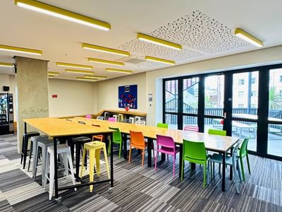 Long communal table with colorful chairs in a modern lounge area at UniLodge Auckland City.