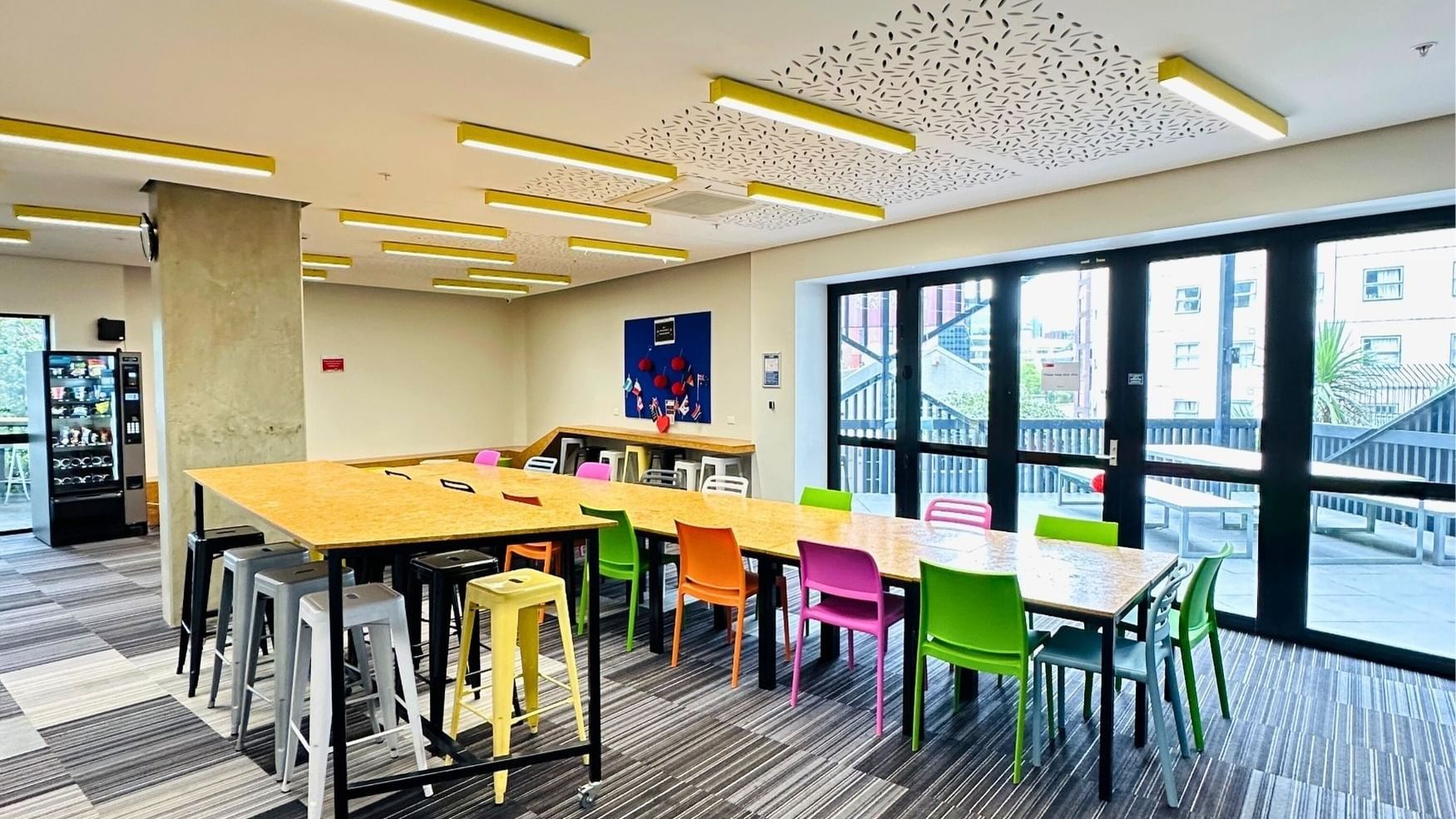 Long communal table with colorful chairs in a modern lounge area at UniLodge Auckland City.