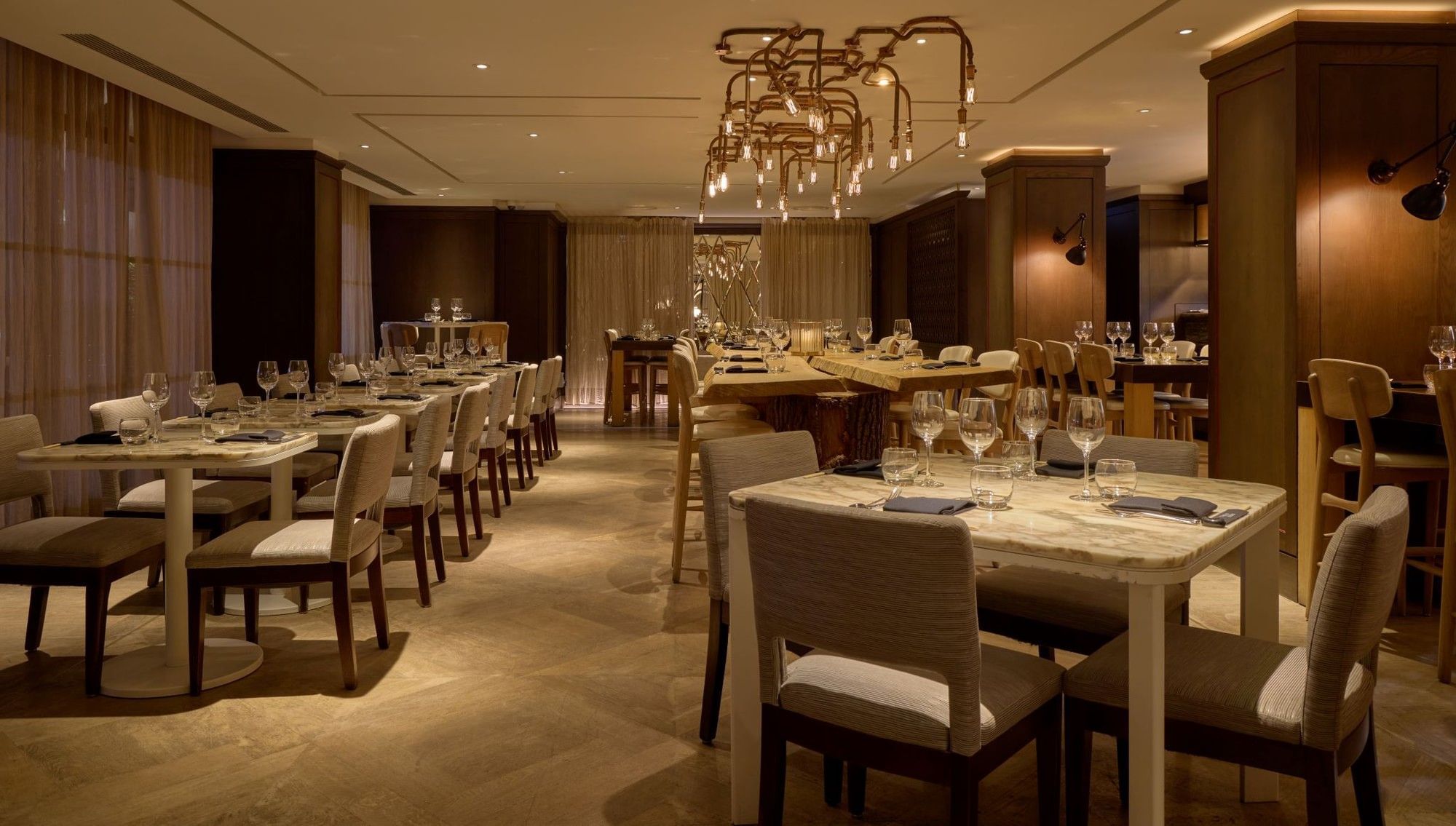 Elegantly decorated May Fair Kitchen restaurant with long dining tables and chairs at The May Fair Hotel, London.