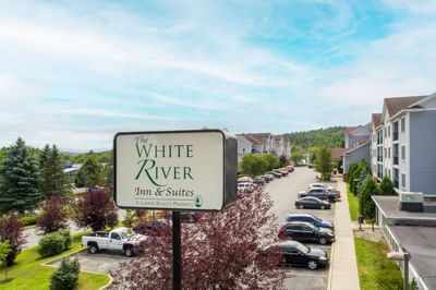 Exterior view of White River Inn & Suites featuring a welcoming sign surrounded by greenery and parked cars