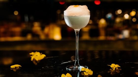 A frothy cocktail in a tall glass on a dark table at The Kitchens