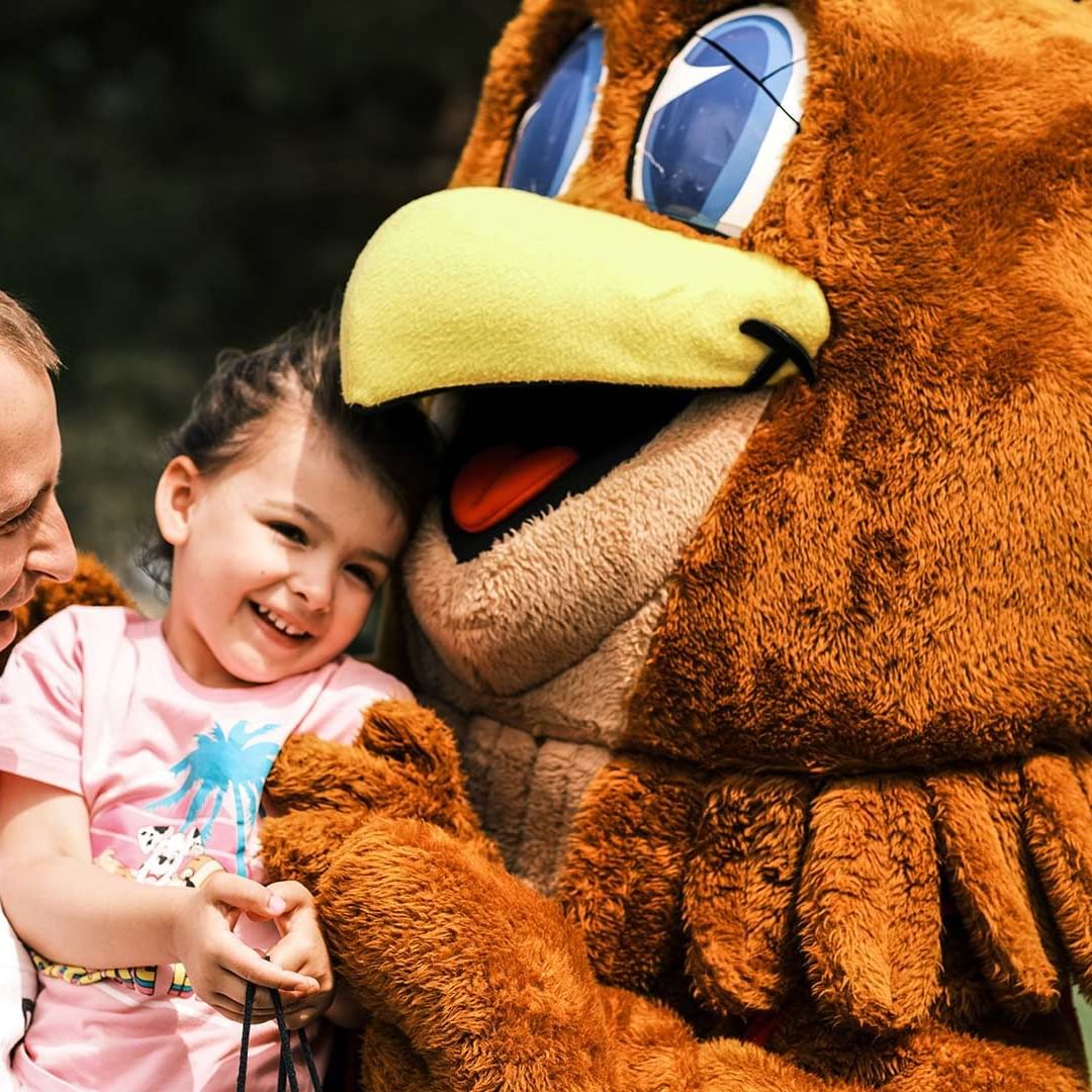 Person in an eagle mascot costume posing with a child and father near Falkensteiner Club Funimation Borik