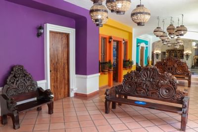 Vestíbulo colorido con paredes moradas, amarillas y turquesas, bancas talladas de madera y lámparas en Los Arcos Suites
