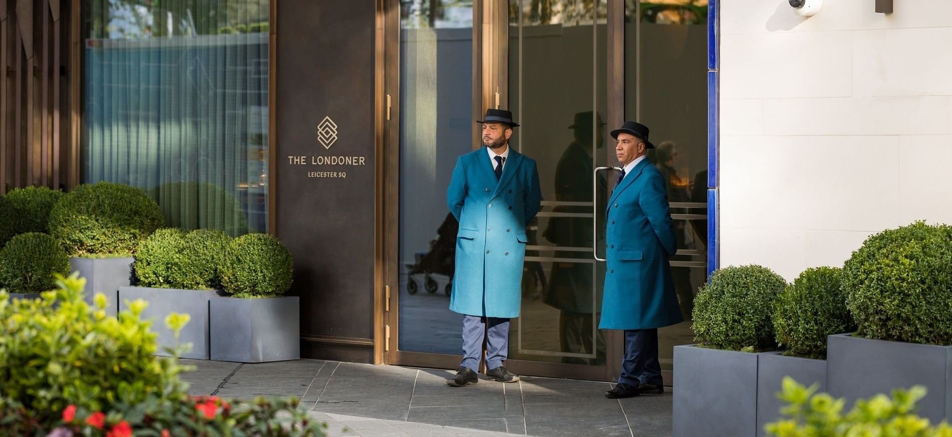 Two doormen in blue uniforms standing at the elegant entrance of The Londoner hotel