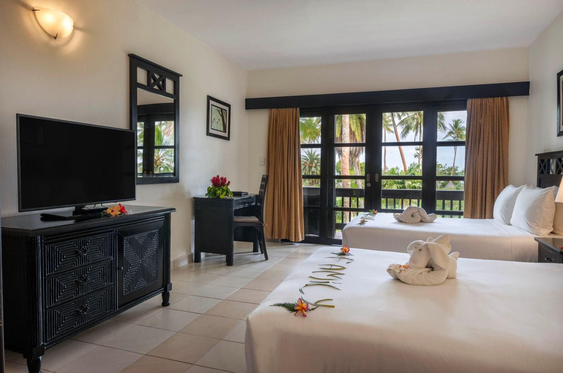 Twin beds by a dark dresser under a wall sconce near a balcony in Ocean View Room at The Naviti Resort - Fiji