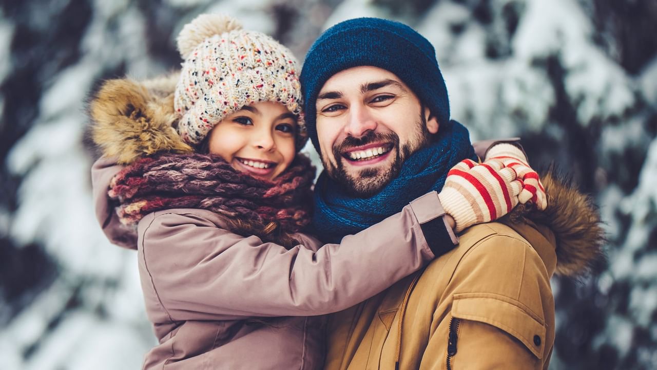 Father holding his daughter, both smiling and wearing winter clothing