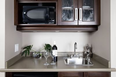 Kitchenette with wine bottle, glasses & pantry with microwave oven in King Superior Den at Retro Suites Hotel