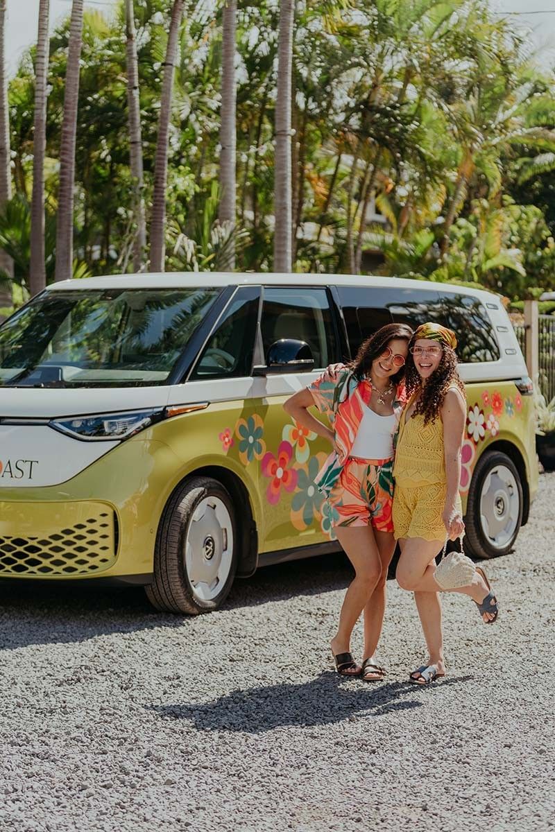 Two women posing next to a yellow van with floral designs