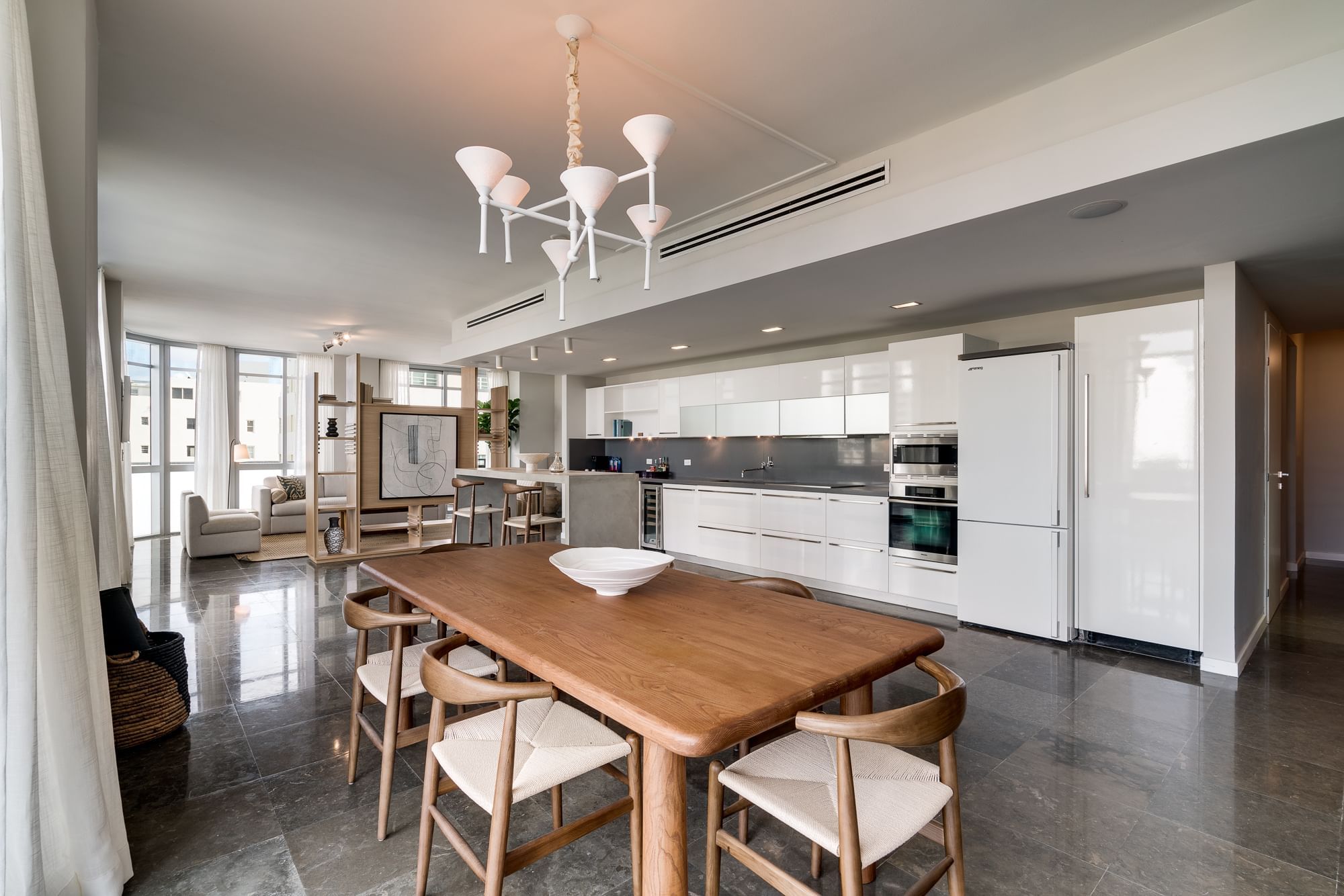 A wide view of a modern kitchen, dining area, and living room in a suite.