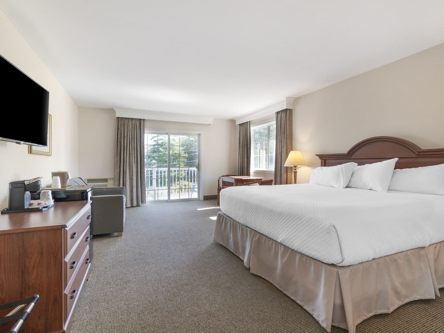 Work desk, seating area, and TV by the cozy bed in One-Bedroom Suites with carpeted floors at Ogunquit Hotel & Suites