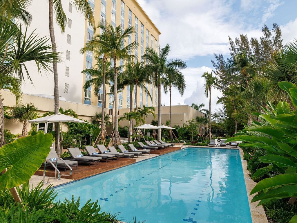 Large pool, lounge chairs, and umbrellas surrounded by palm trees and greenery.