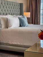 Plush bed with a tufted headboard by a glass table under glowing lamps in Presidential Suite at Warwick Melrose Dallas