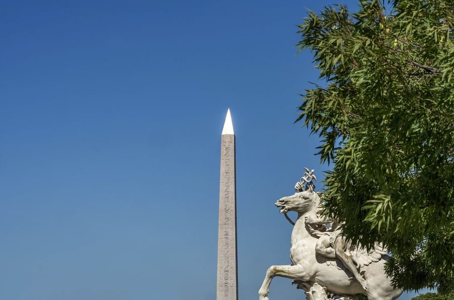 White horse statue standing by a tall obelisk under a clear blue sky near Hotel Westminster Paris