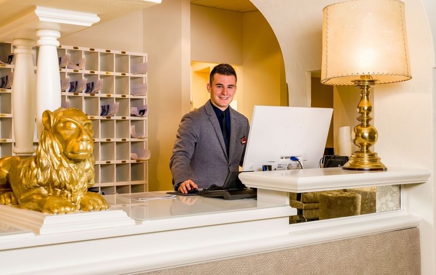 Ein Hotelmitarbeiter steht an der Rezeption und begrüßt Gäste mit einem freundlichen Lächeln.