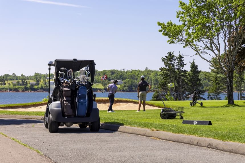 Golfers standing on a green path by a sand bunker near a blue body of water backdrop at Rodd Brudenell River Resort
