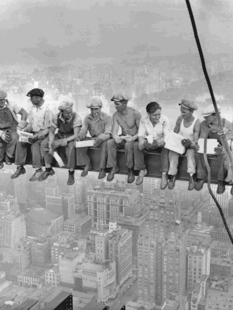 Historical photo of ironworkers eating lunch on a steel beam high above New York City