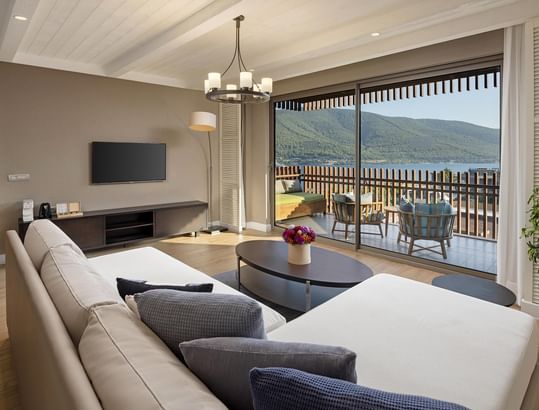 Family Suite's living room with sectional sofa, coffee table, TV, balcony, and scenic outdoor view.