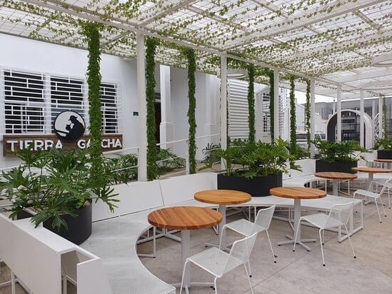 Outdoor seating area of Tierra Gacha with wooden tables, chairs and lush greenery under trellised canopy near D Sabana Hotel