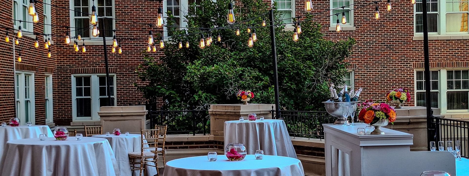 Cocktail tables by a white bar under string lights in The Bridewell Suite at Warwick Melrose Dallas