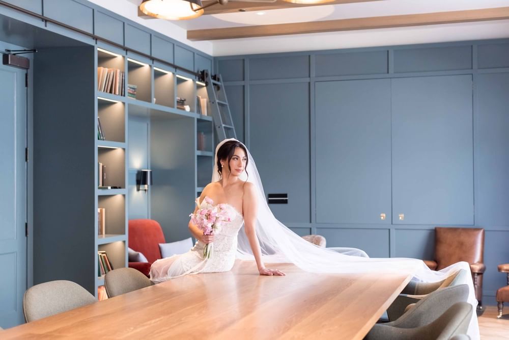 Beautiful bride in a flowing gown with a pink bouquet, posing in a chic room at El Prado Hotel