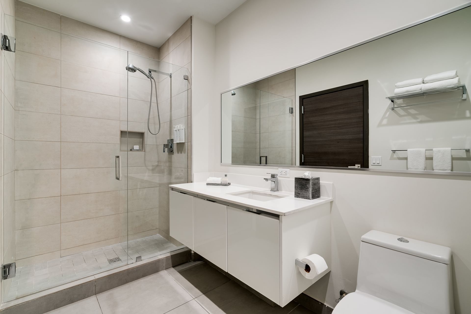 A modern bathroom with a glass-enclosed shower, floating sink, and toilet.