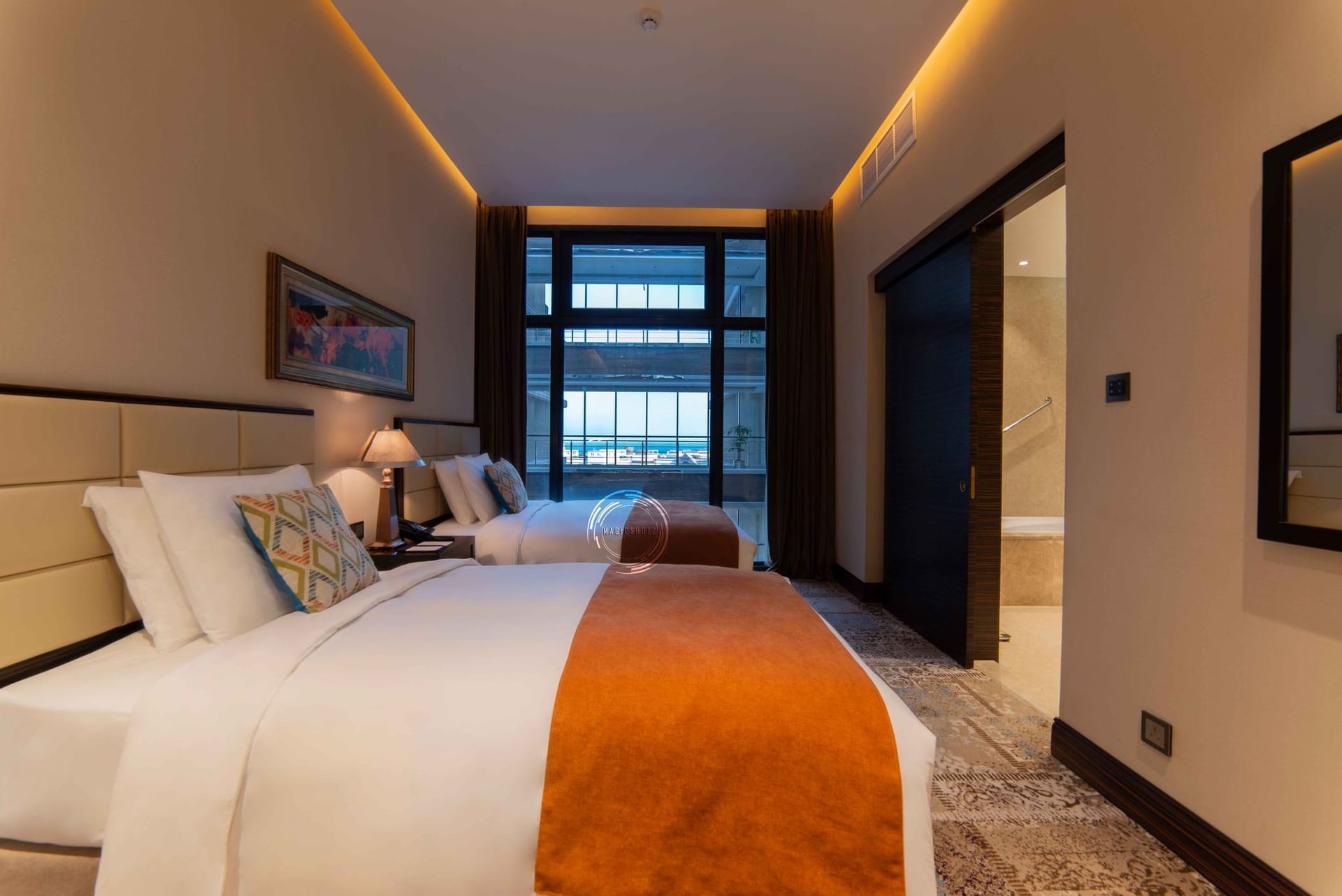 Two twin beds by a lamp under a window overlooking a balcony in Superior Twin Room at Warwick Al Khobar