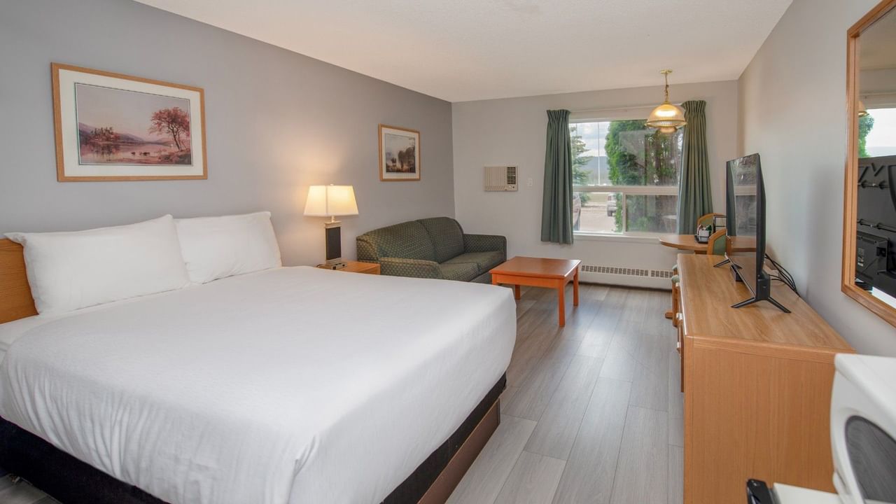 A hotel room with a bed, couch, coffee table, lamp, TV, and two framed pictures.