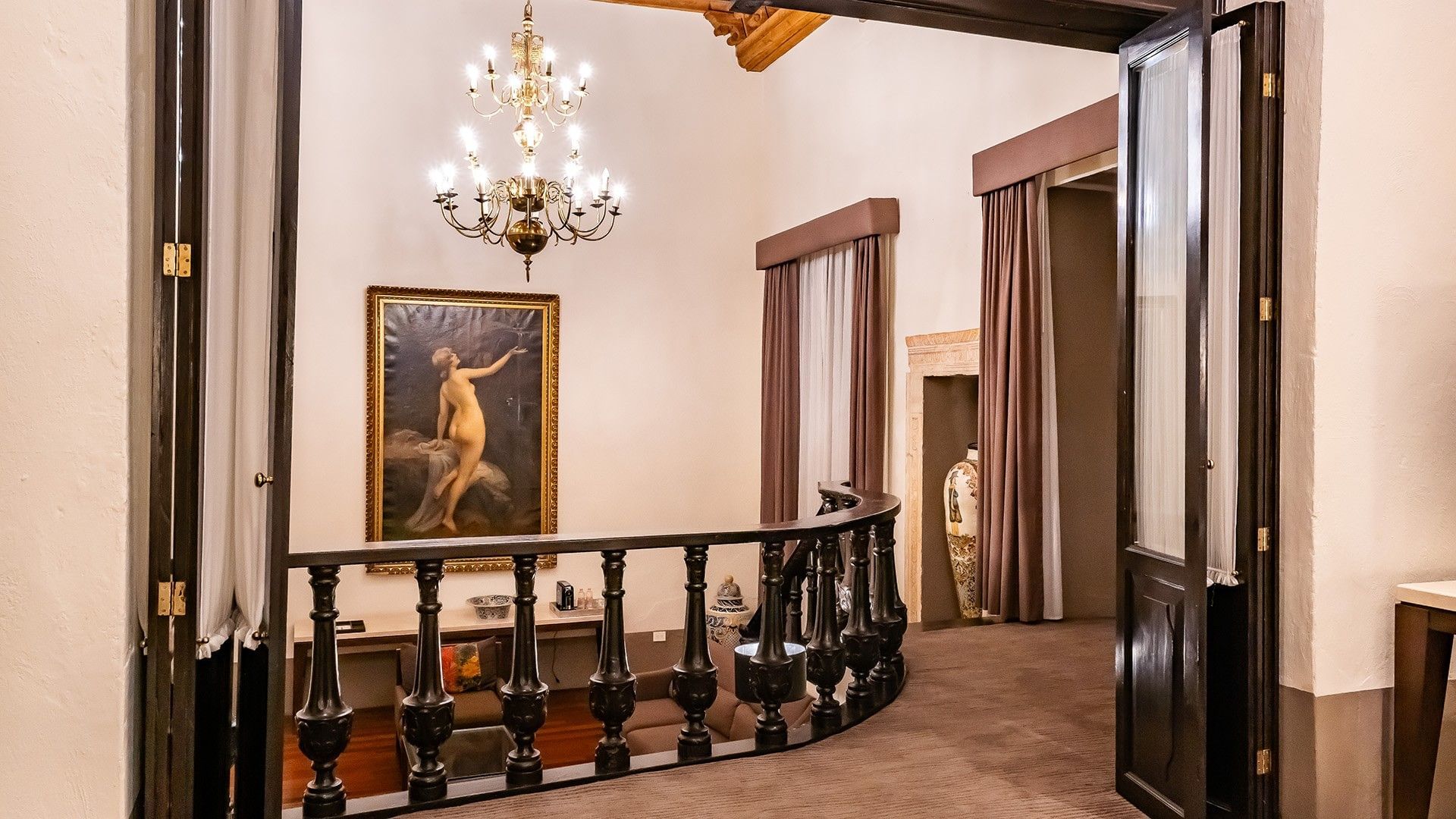 King Presidential Suite balcony with a dark wood railing, gold chandelier, and classic artwork at Quinta Real Puebla