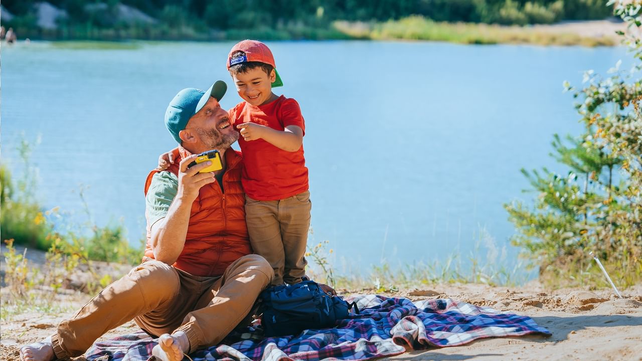 Father and son sharing a moment by the lake on a plaid blanket in Calgary