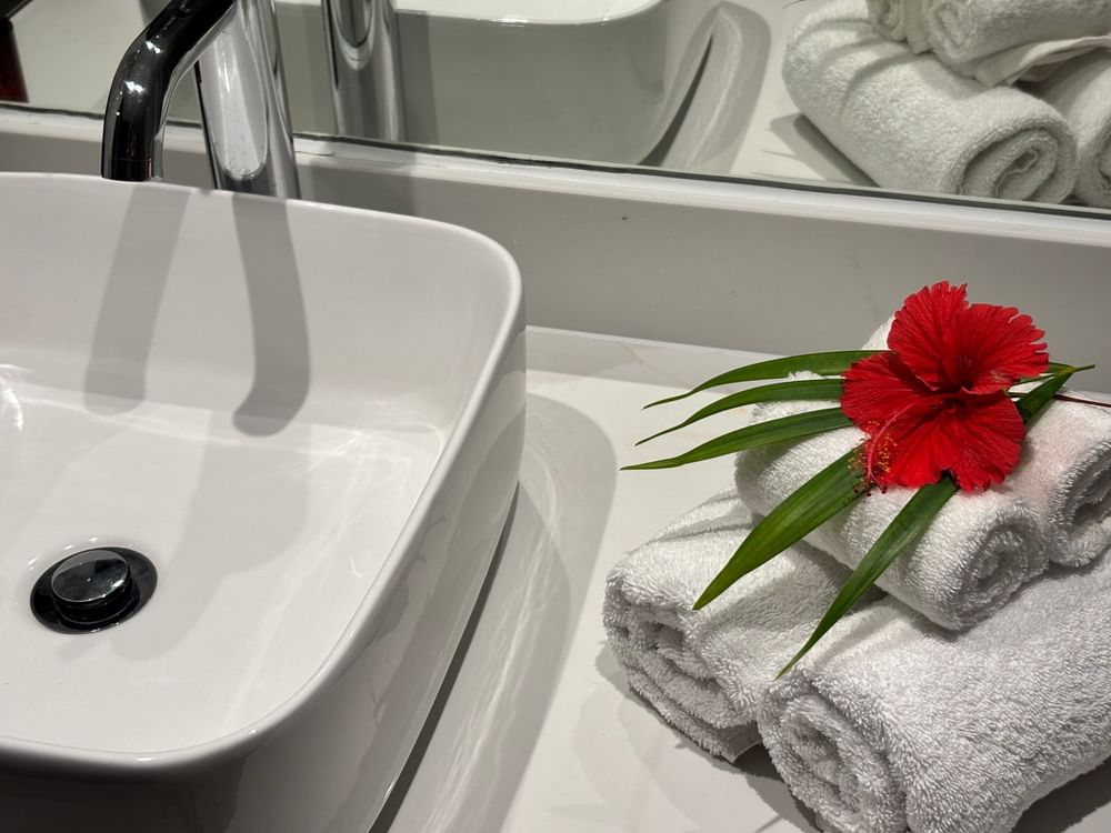 A bathroom sink with a red flower on towels in an Ocean View Two Double Room at Warwick Fiji, Korolevu.