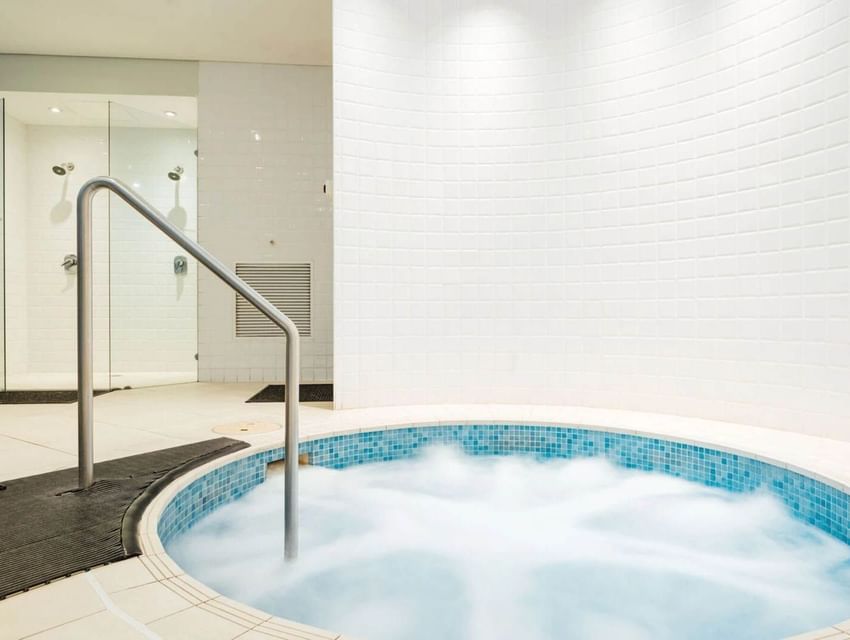 Indoor jacuzzi with warm lighting and shower compartments behind at Paradox Sydney cbd hotels with indoor pool