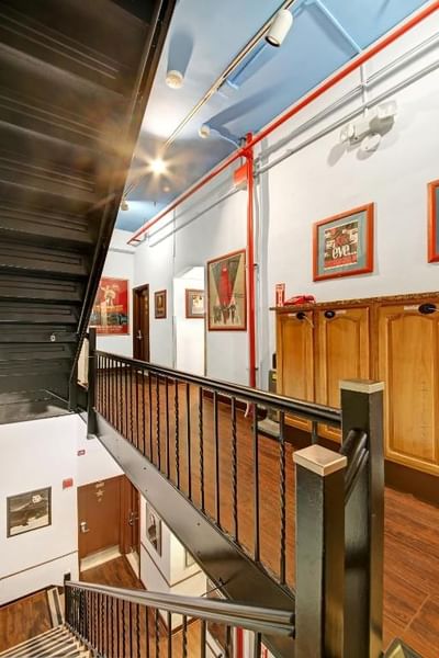 Chelsea Pines Inn stairs with metal railings and wooden floors leading to a hallway with wooden cabinets and framed pictures.