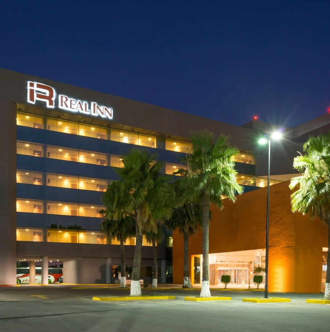 Exterior of Real Inn Nuevo Laredo at night, showing the illuminated building, palm trees, and the hotel entrance