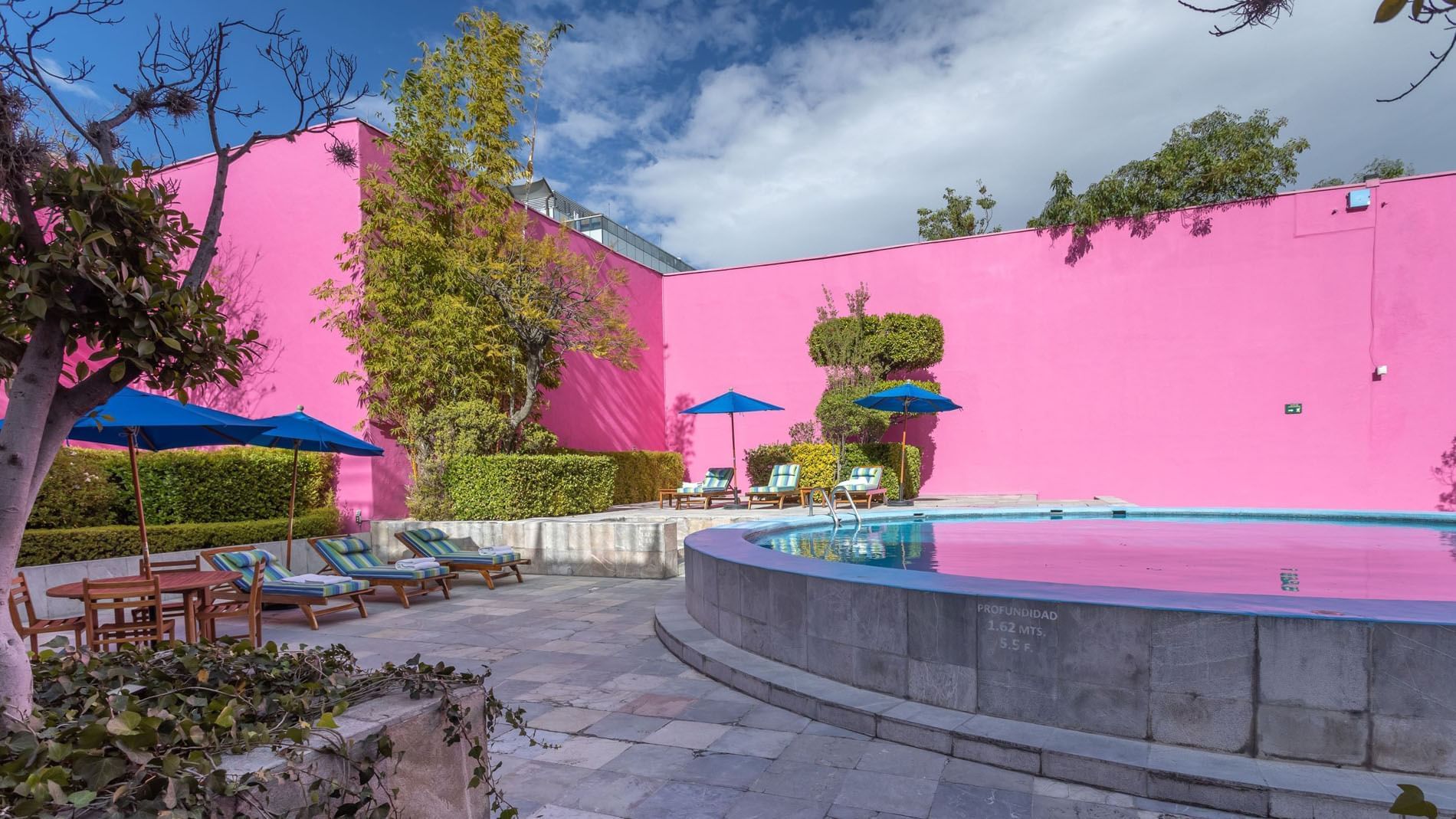 King Chapultepec Suite circular pool surrounded by pink walls, green trees, and blue umbrellas at Camino Real Polanco Mexico