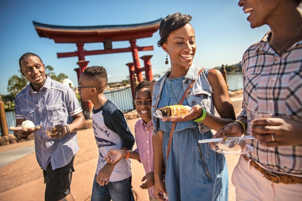 A family with three boys pass by a Japanese-inspired arch, holding plates of food and drinks.