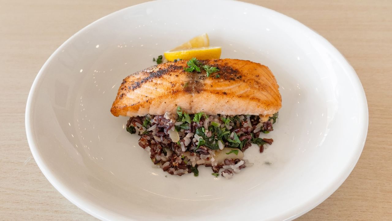 A grilled salmon fillet atop a bed of greens, garnished with herbs and lemon slices.