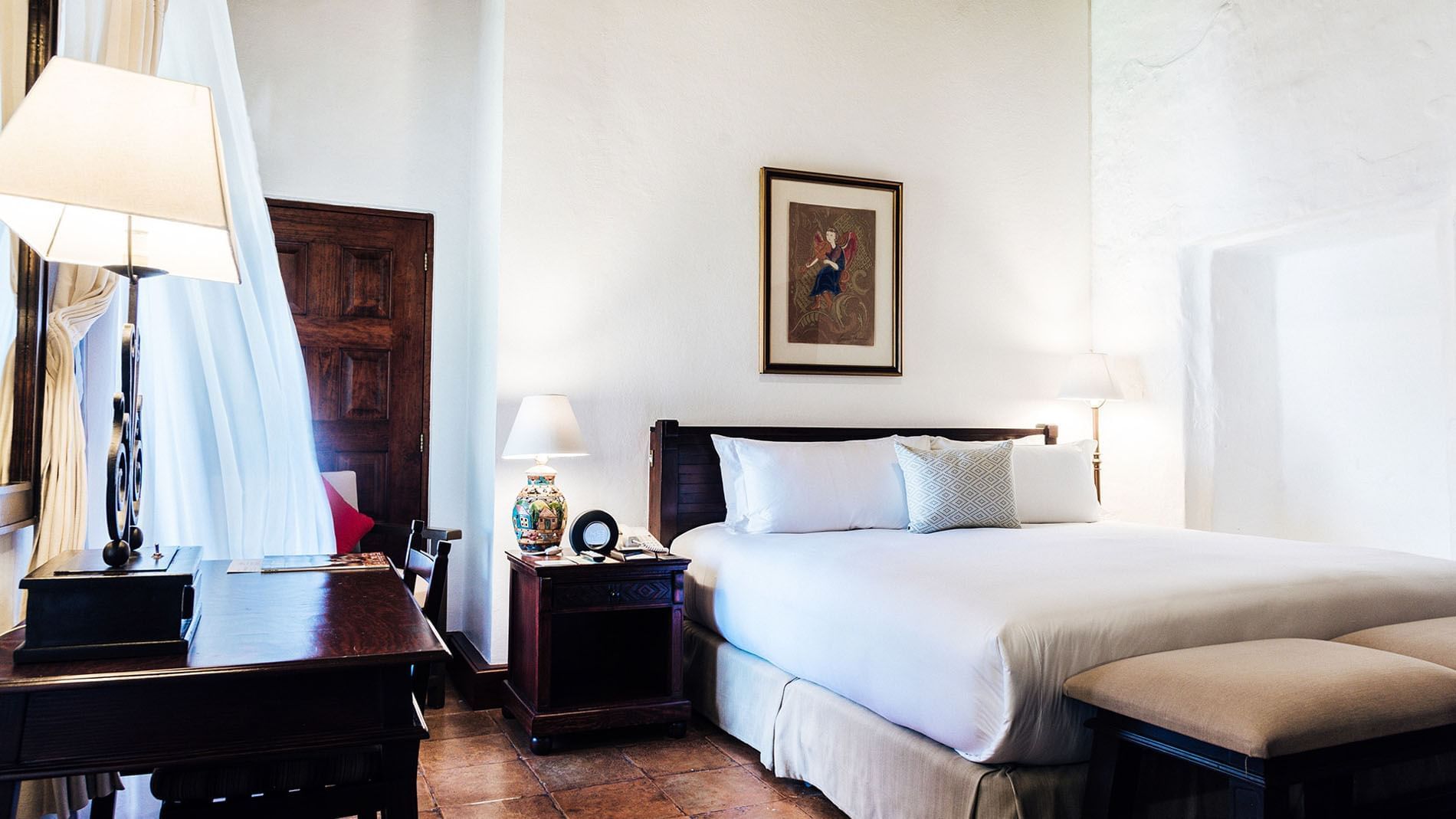 Work desk, ottoman, and nightstand by the cozy bed in the King Grand Class Suite at Quinta Real Oaxaca