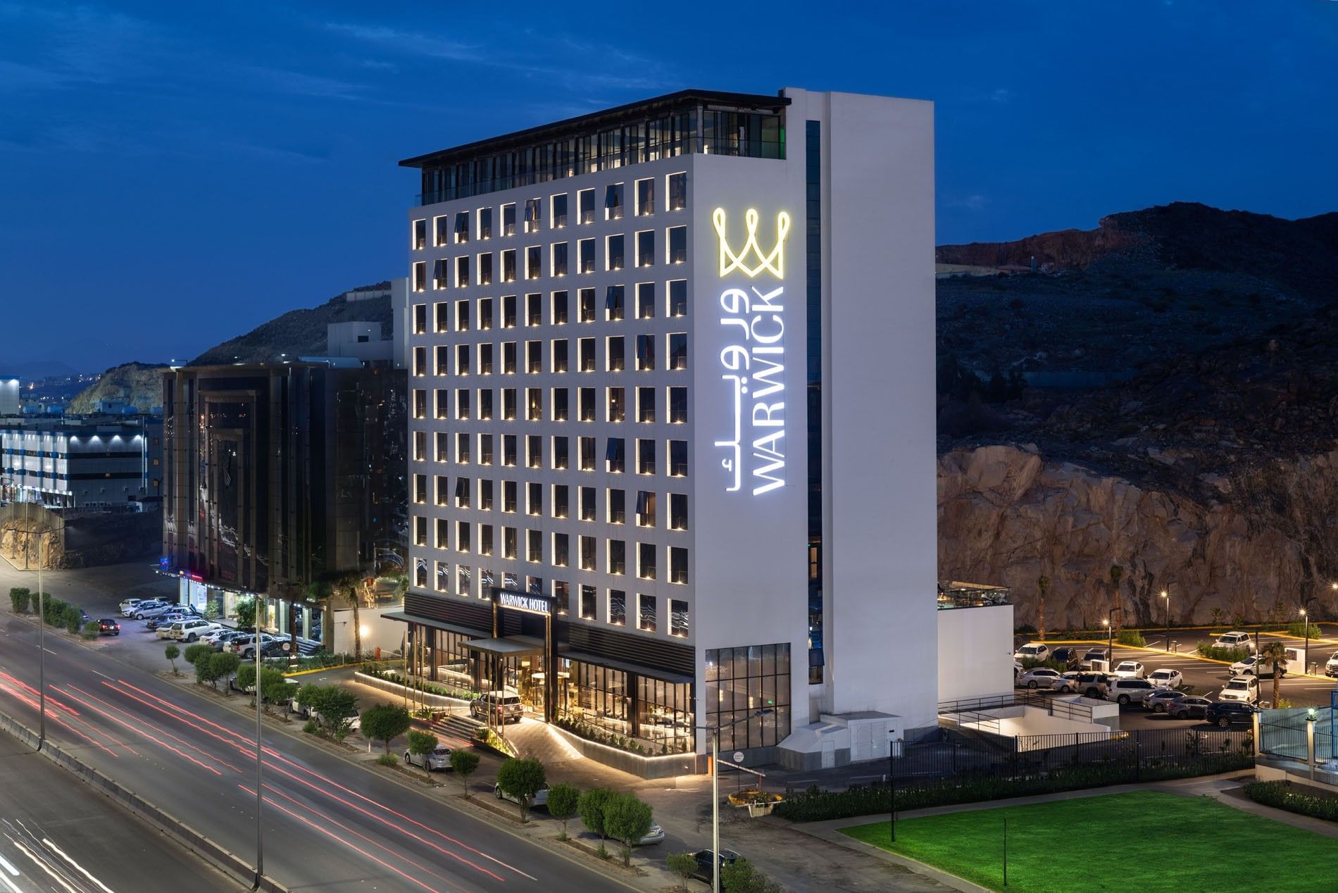 Exterior view of the Warwick Al Taif Hotel at night with illuminated signage and surrounding urban landscape