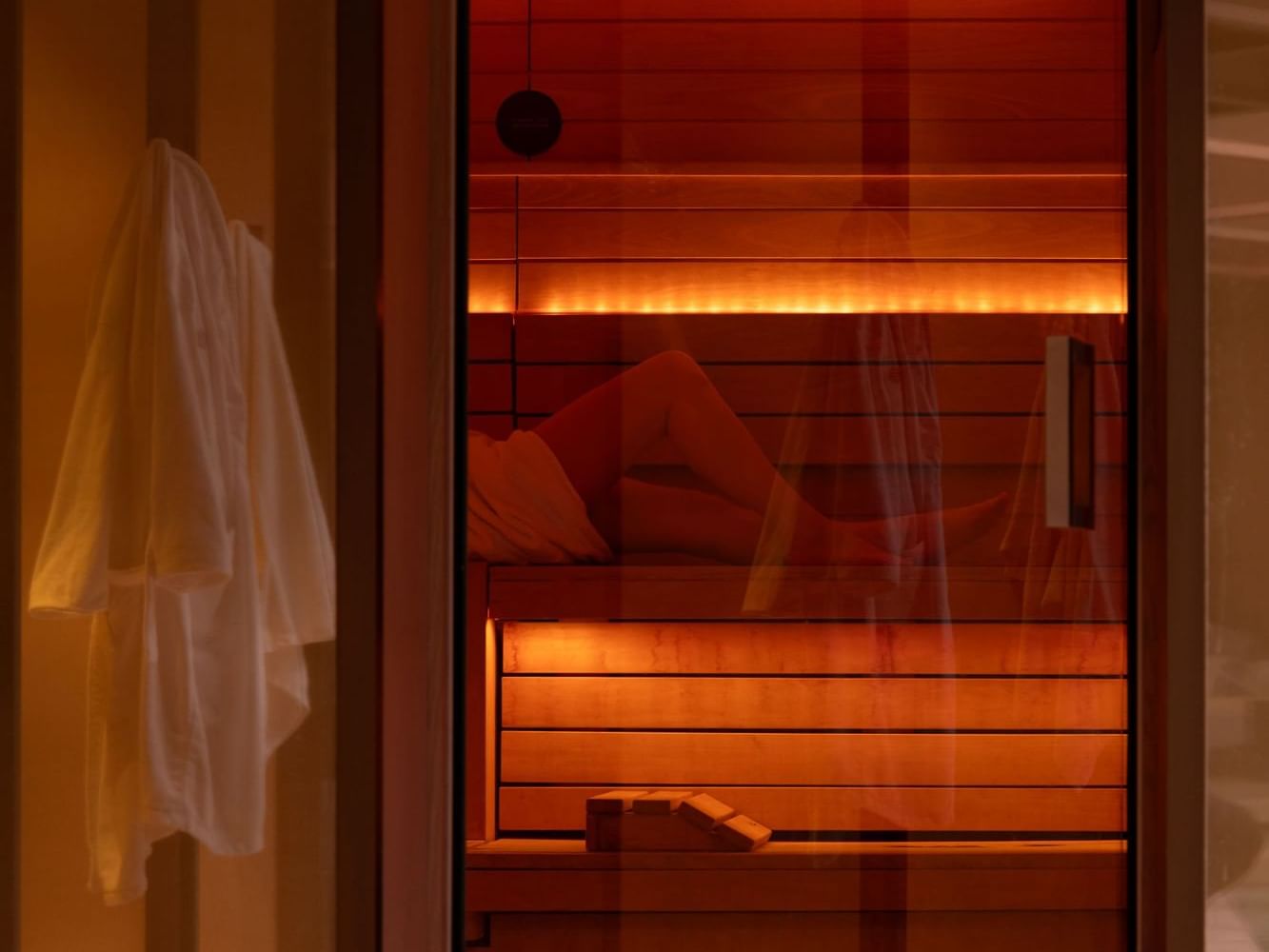 Warmly lit sauna with a person relaxing inside at The Londoner Hotel