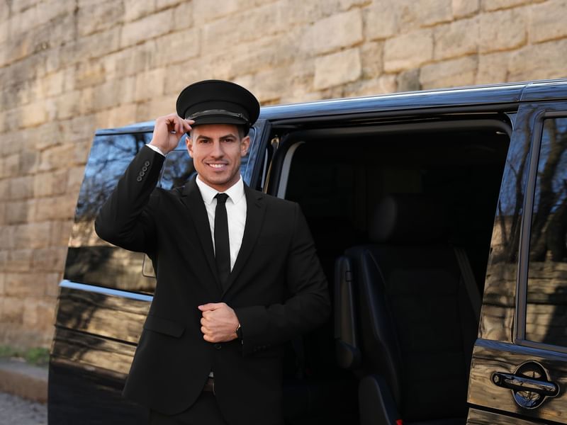 Chauffeur in a suit and cap stands beside a luxury van, preparing to assist passengers at The Banjaran Hotsprings Retreat