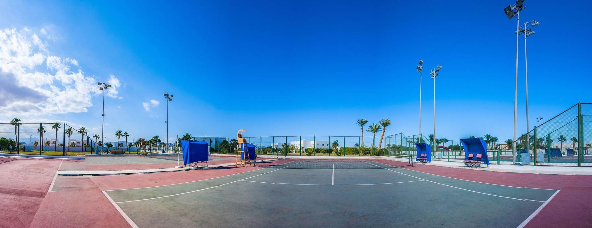 Panoramic view of tennis court surrounded by palm trees with seating areas & floodlights at Pickalbatros Golf Beach Resort