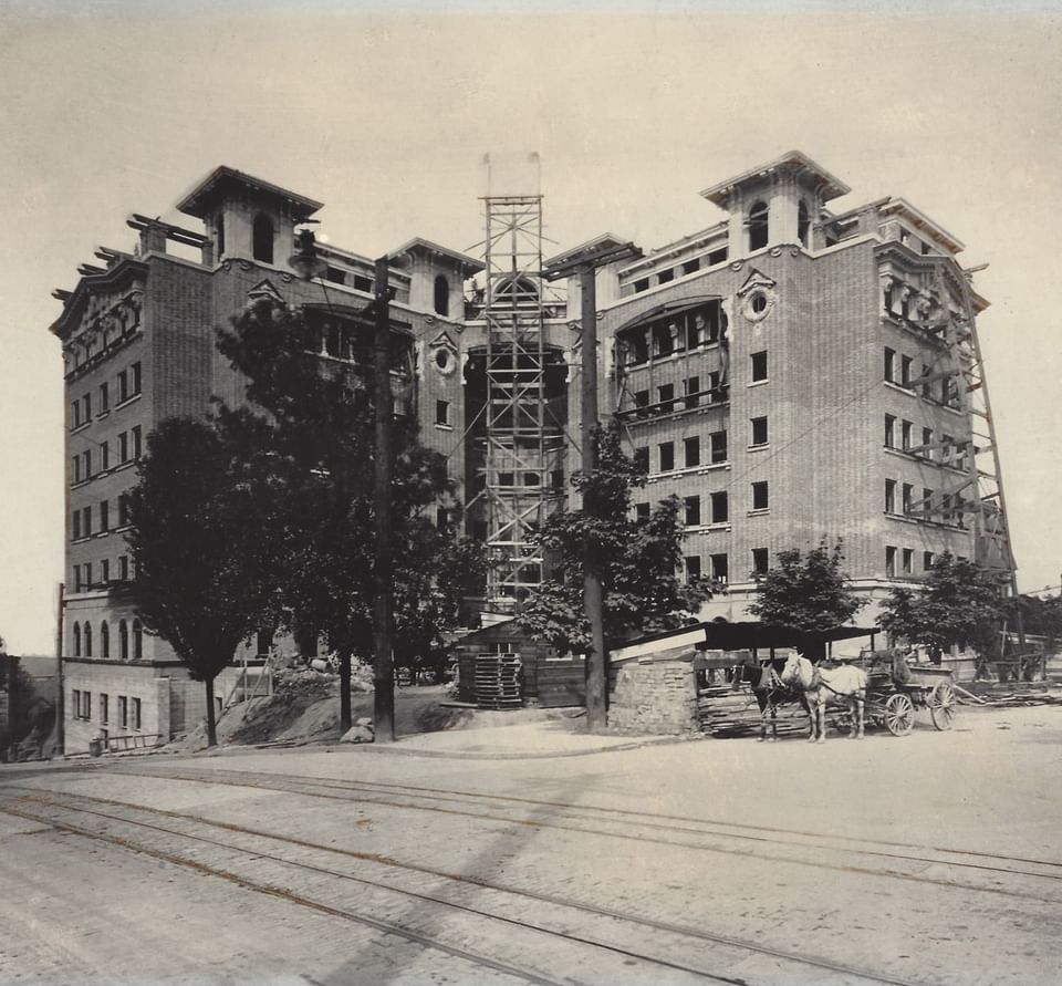 Vintage image of Hotel Sorrento under construction, with scaffolding, trees, and a horse-drawn carriage out front