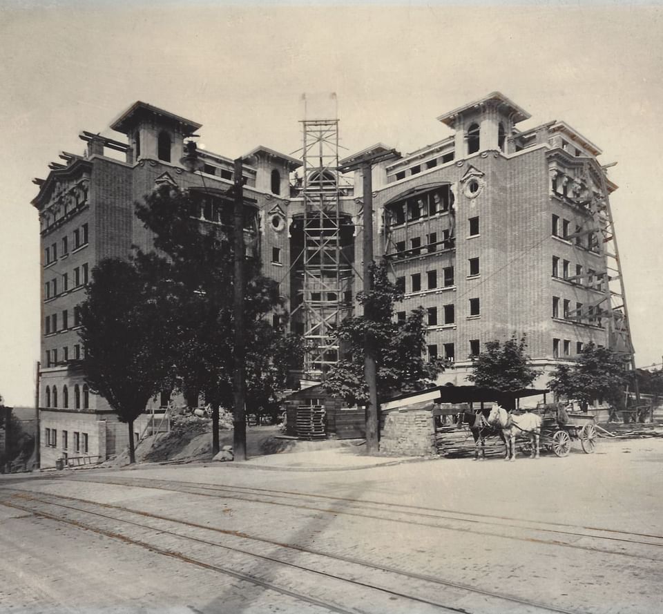 Vintage image of Hotel Sorrento under construction, with scaffolding, trees, and a horse-drawn carriage out front