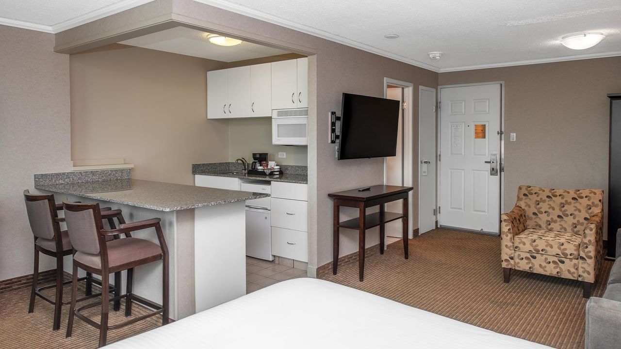 Hotel suite with a kitchenette, dining table, wall-mounted TV and sitting area.