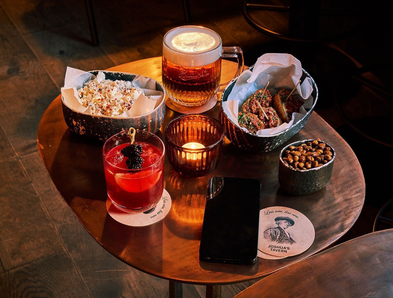 Appetizers served with a cocktail and a glass of beer on a wooden table at Joshua's Tavern in The Londoner Hotel