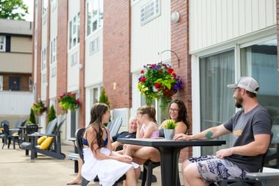 Family sitting at an outdoor patio table talking and relaxing outside a brick guest room wing at Rodd Moncton