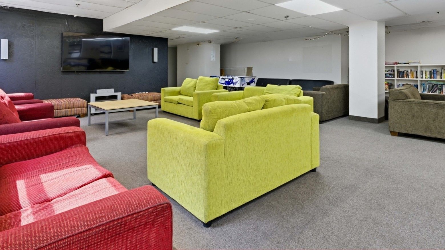 Lounge area with yellow and red couches, bookshelves, and a TV at UniLodge Stafford House.